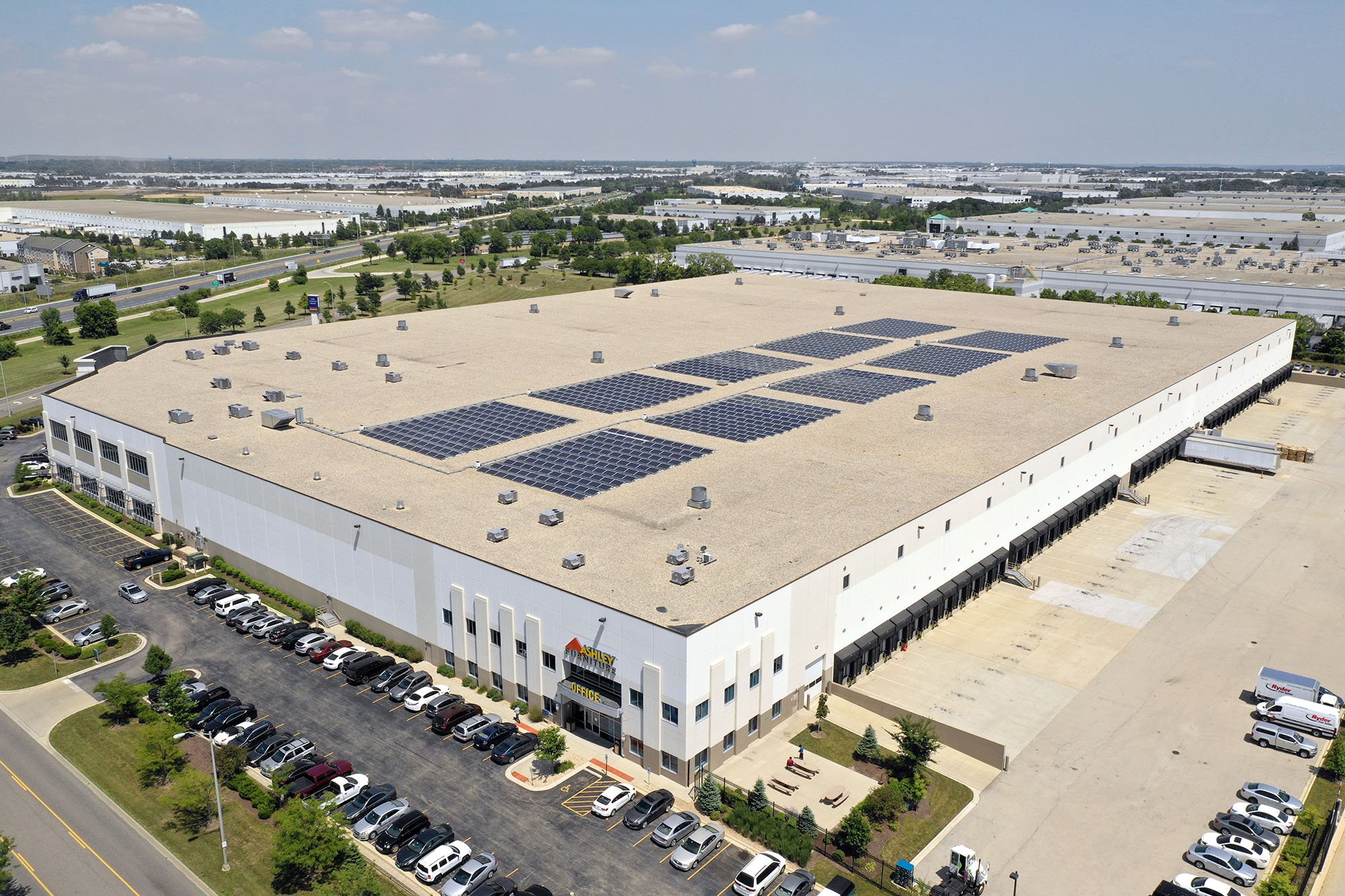 An Ashley Furniture Industries building with rooftop solar panels, with their company logo in the top right-hand corner, representing one of SunPeak’s commercial solar power projects. 